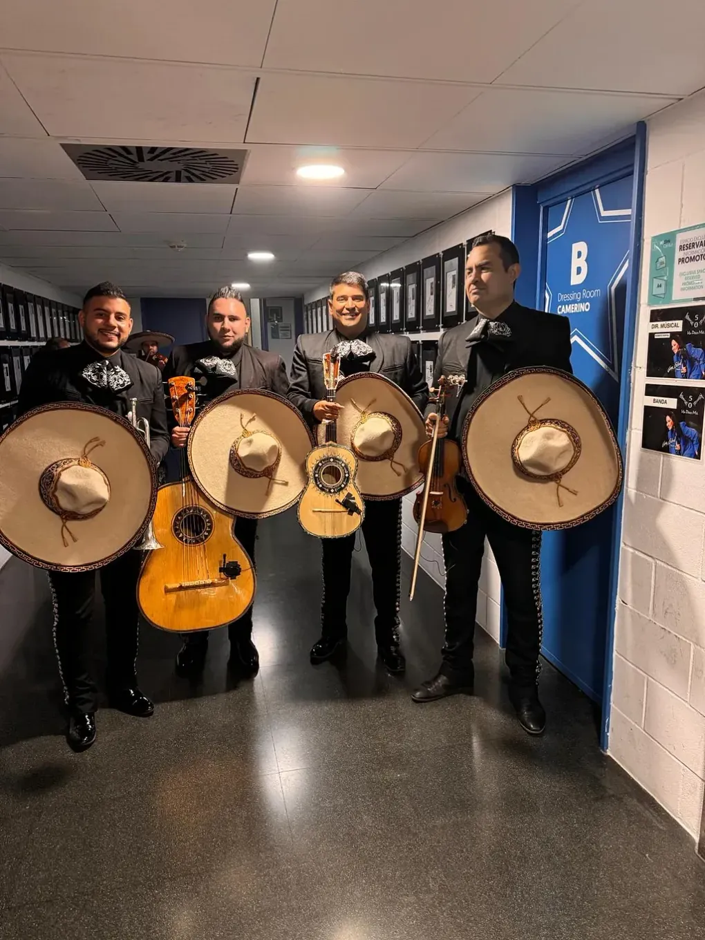 Un grupo de hombres están de pie en un pasillo sosteniendo guitarras y sombreros.