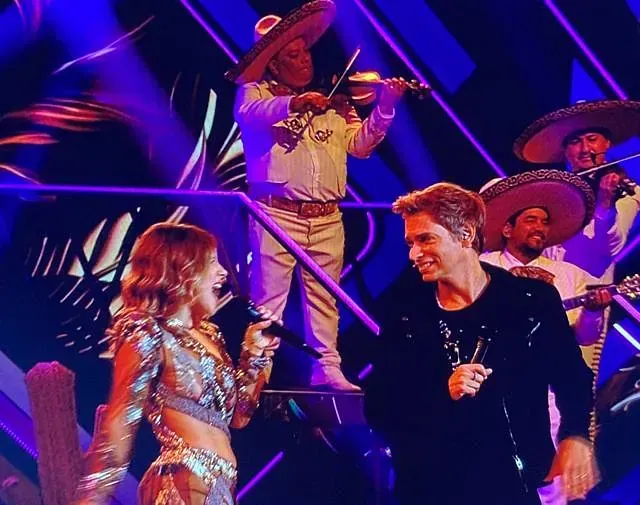 Una mujer cantando en un micrófono mientras un hombre toca un violín.