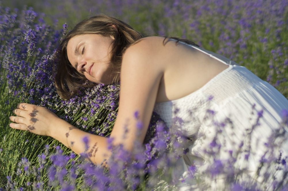 Una persona vestida de blanco descansa plácidamente entre flores de lavanda moradas en un campo.