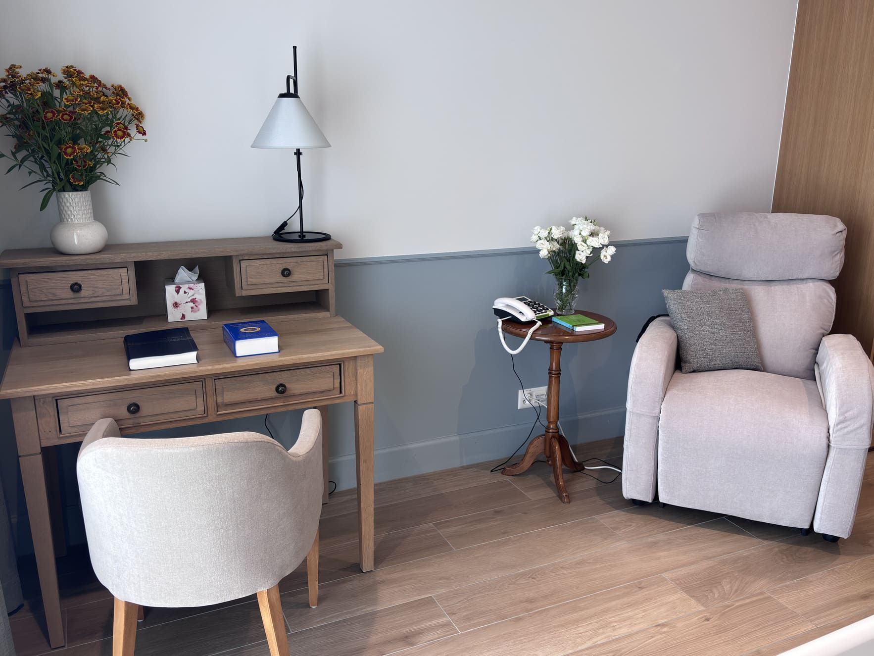 Bureau en bois et fauteuil cosy dans une chambre lumineuse de la Maison Le Verger à Bursins, fleurs décoratives