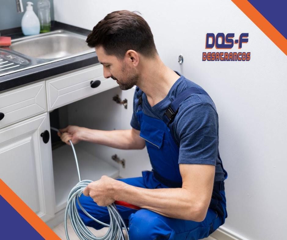 Un hombre está arrodillado debajo de un fregadero sosteniendo una manguera.