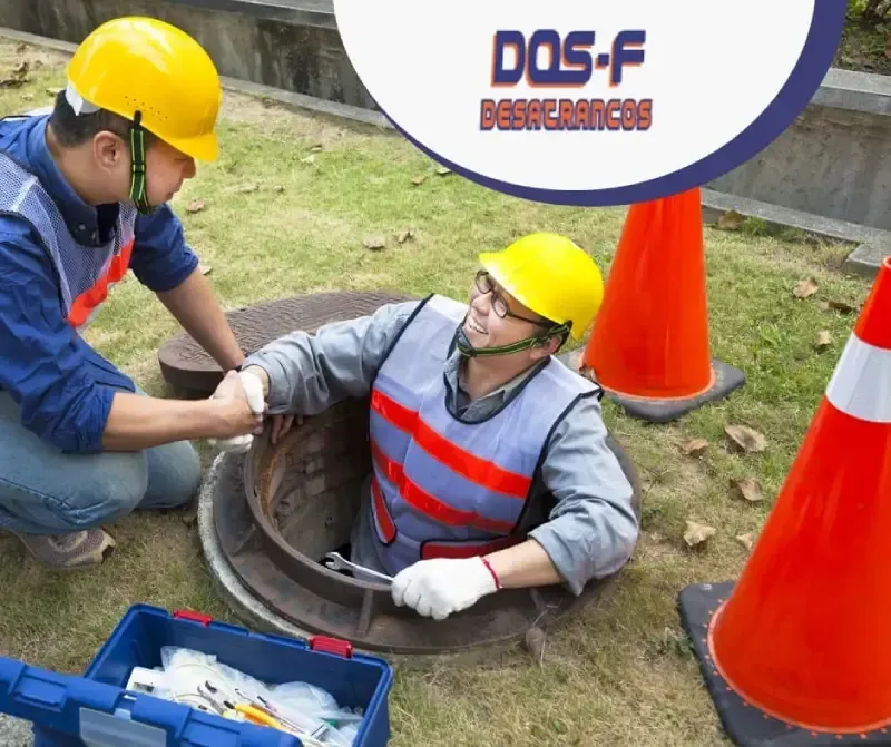 Dos hombres con cascos de seguridad están trabajando en una tapa de alcantarilla.