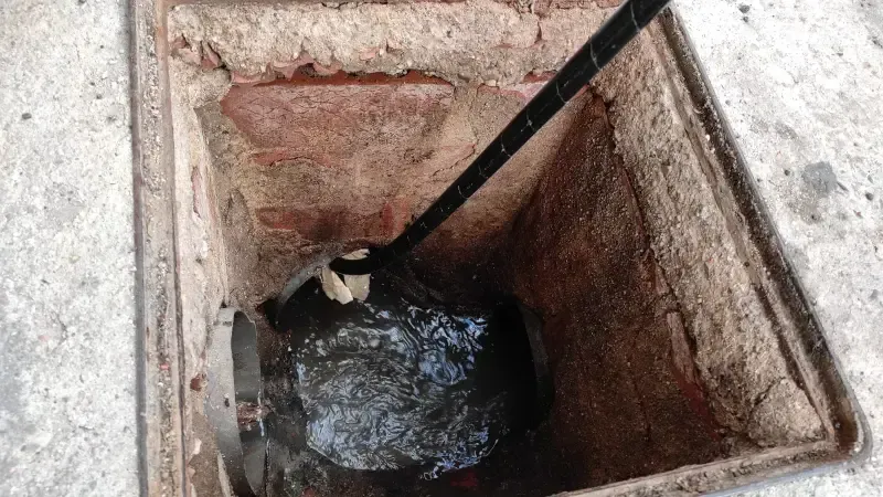Una tapa de alcantarilla por la que sale agua y de la que sobresale una manguera.
