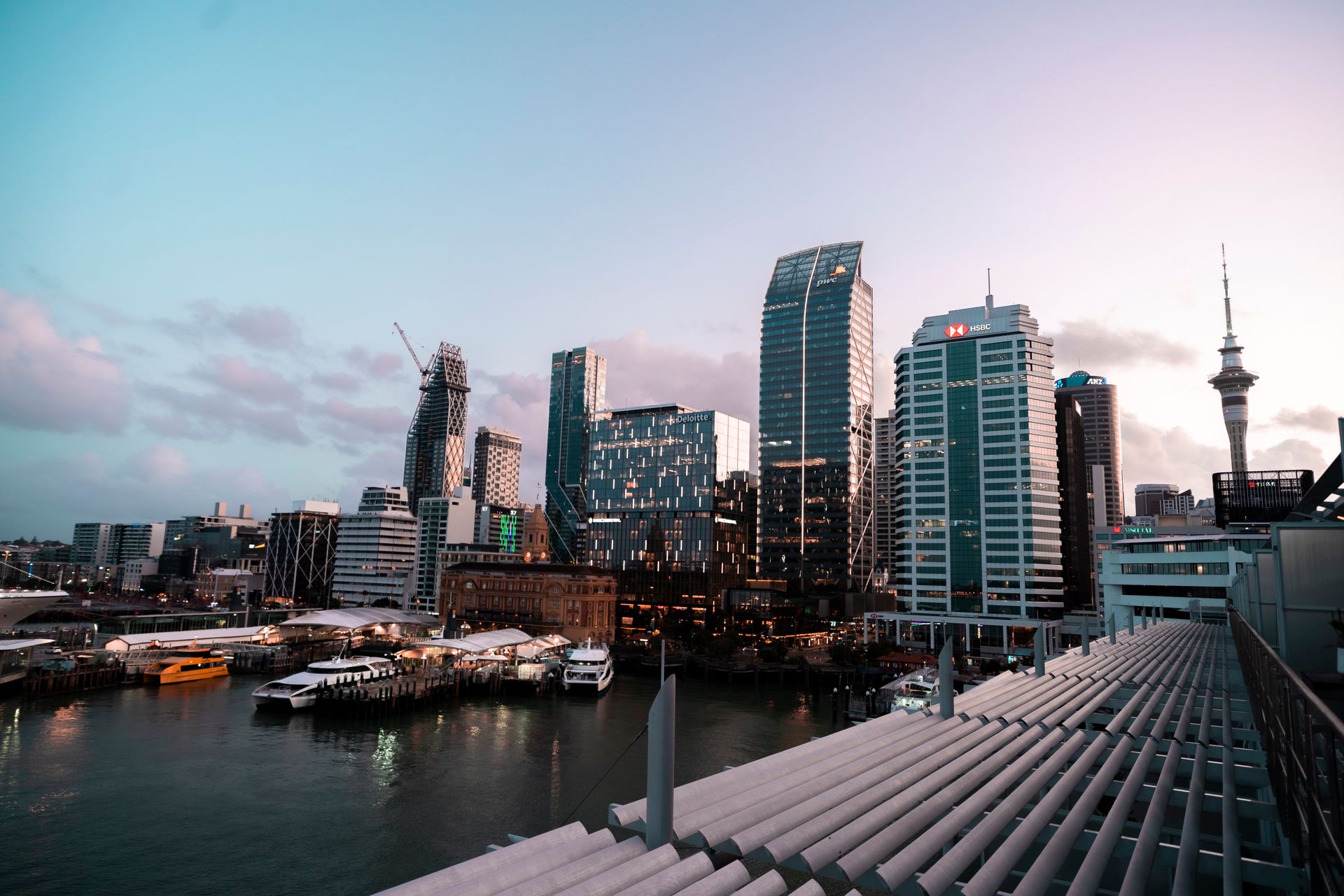 City skyline at dusk, with harbour, buildings, and Sky Tower visible.
