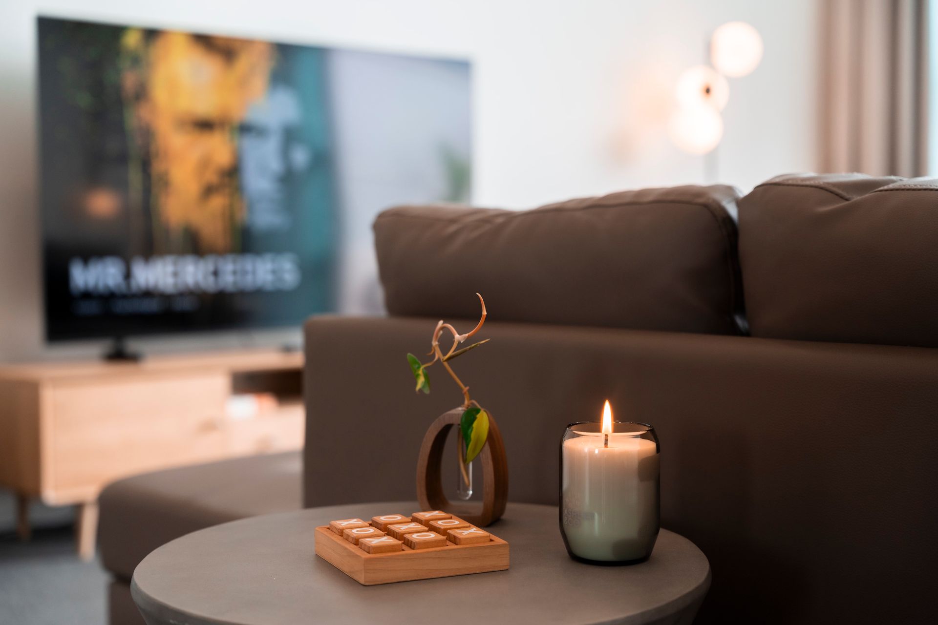 Living room with a lit candle, a small vase with twigs, and a TV showing 