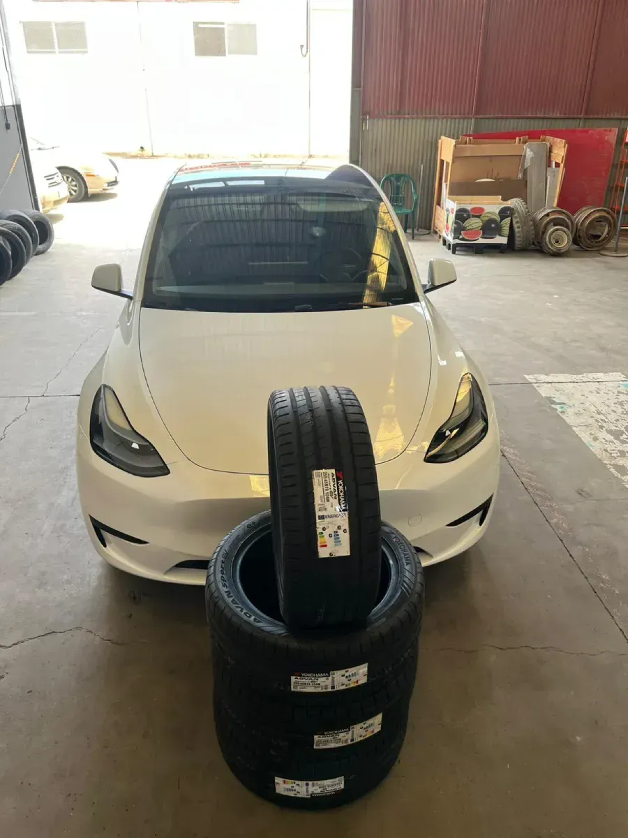Tesla Model Y de color blanco, con neumáticos apilados en el frente, dentro de un garaje.