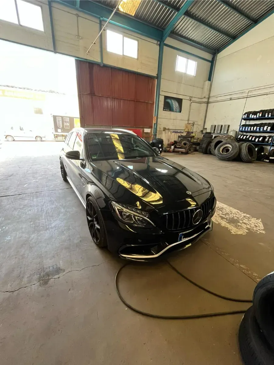 Un Mercedes-Benz sedán negro aparcado en un garaje abierto. El coche es brillante y refleja la luz.