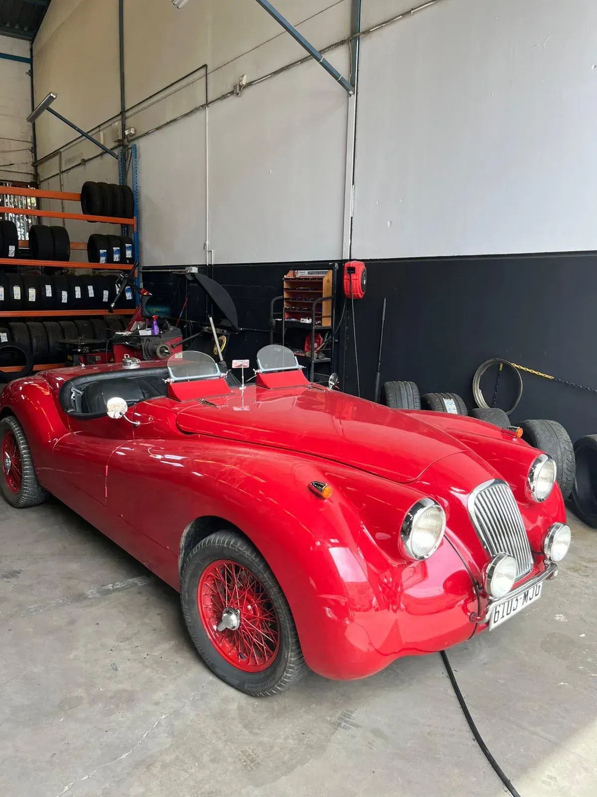 Coche clásico descapotable de color rojo en garaje con neumáticos y equipamiento visibles.