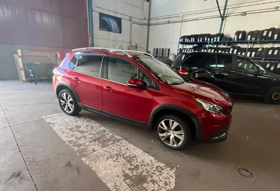 Peugeot 2008 SUV de color rojo, estacionado en el interior de un garaje, al lado de un todoterreno negro y neumáticos.