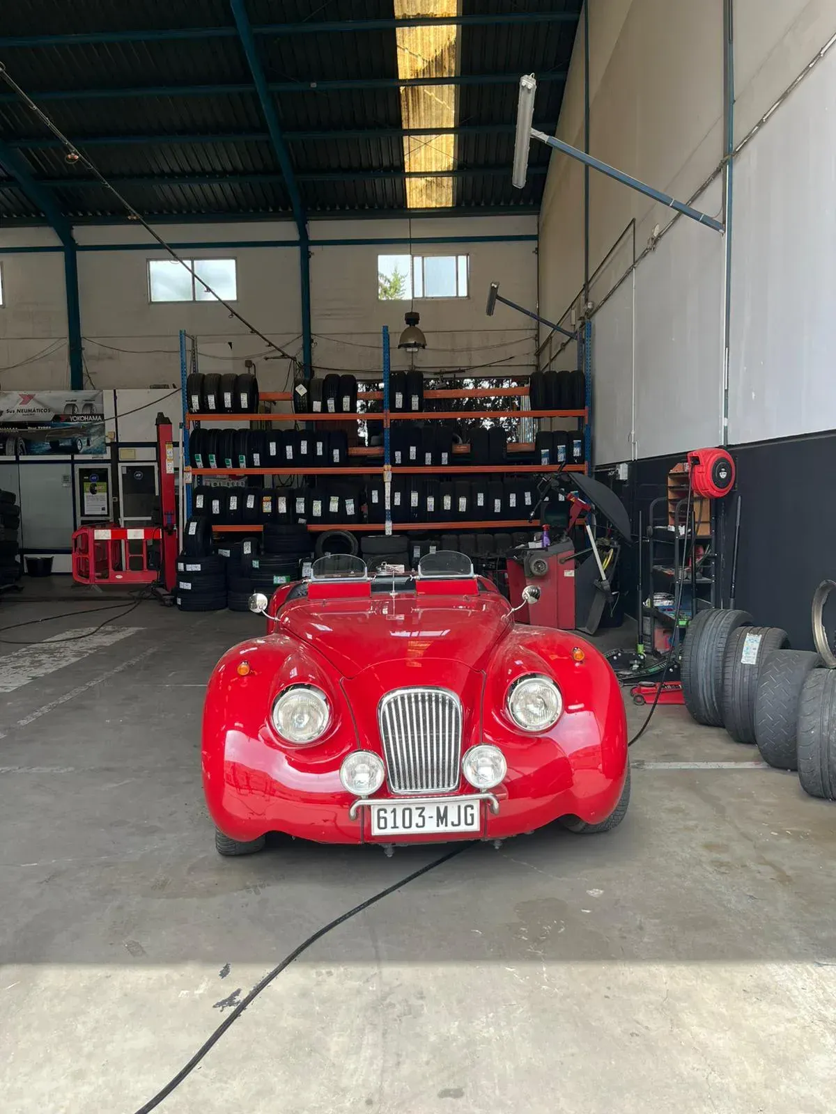 Coche antiguo rojo en un garaje con neumáticos en los estantes.
