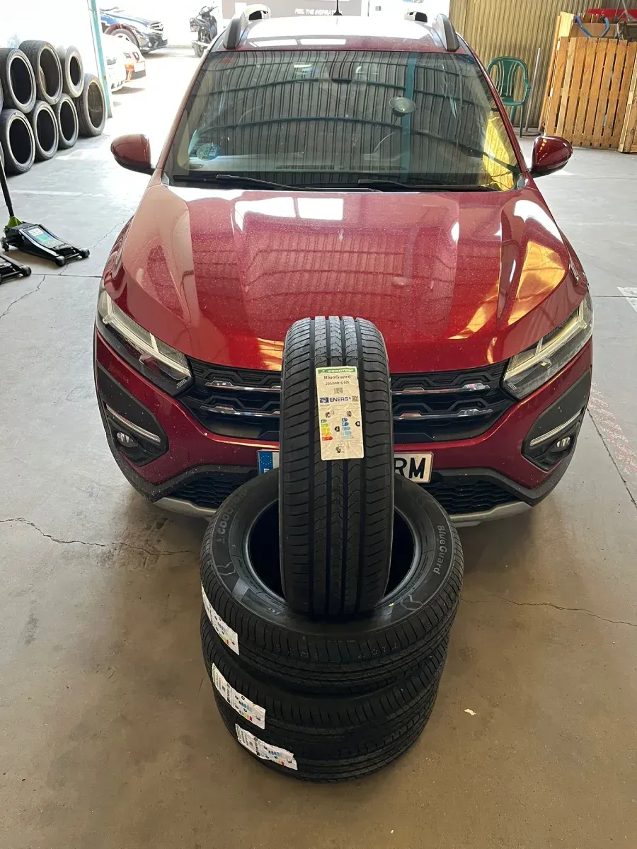 Coche rojo con una pila de neumáticos nuevos en un garaje.