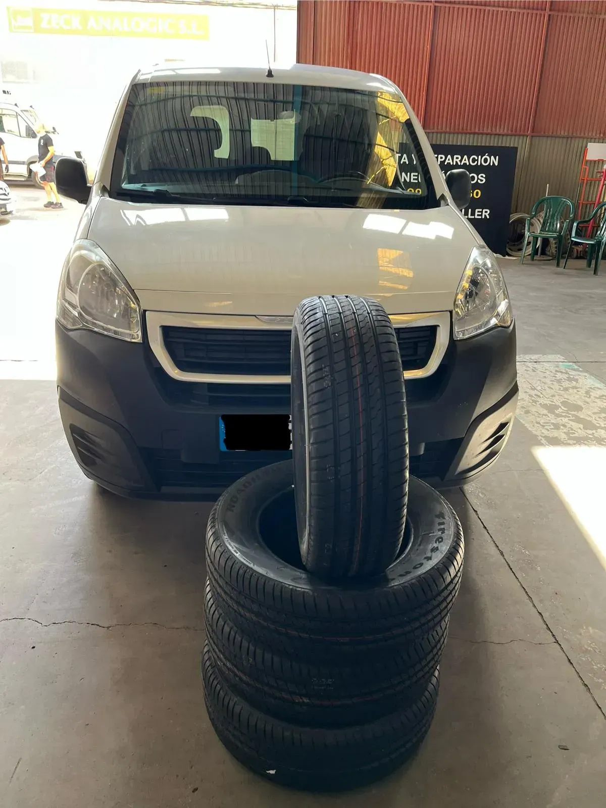 Furgoneta blanca con una pila de neumáticos negros delante, en el interior.