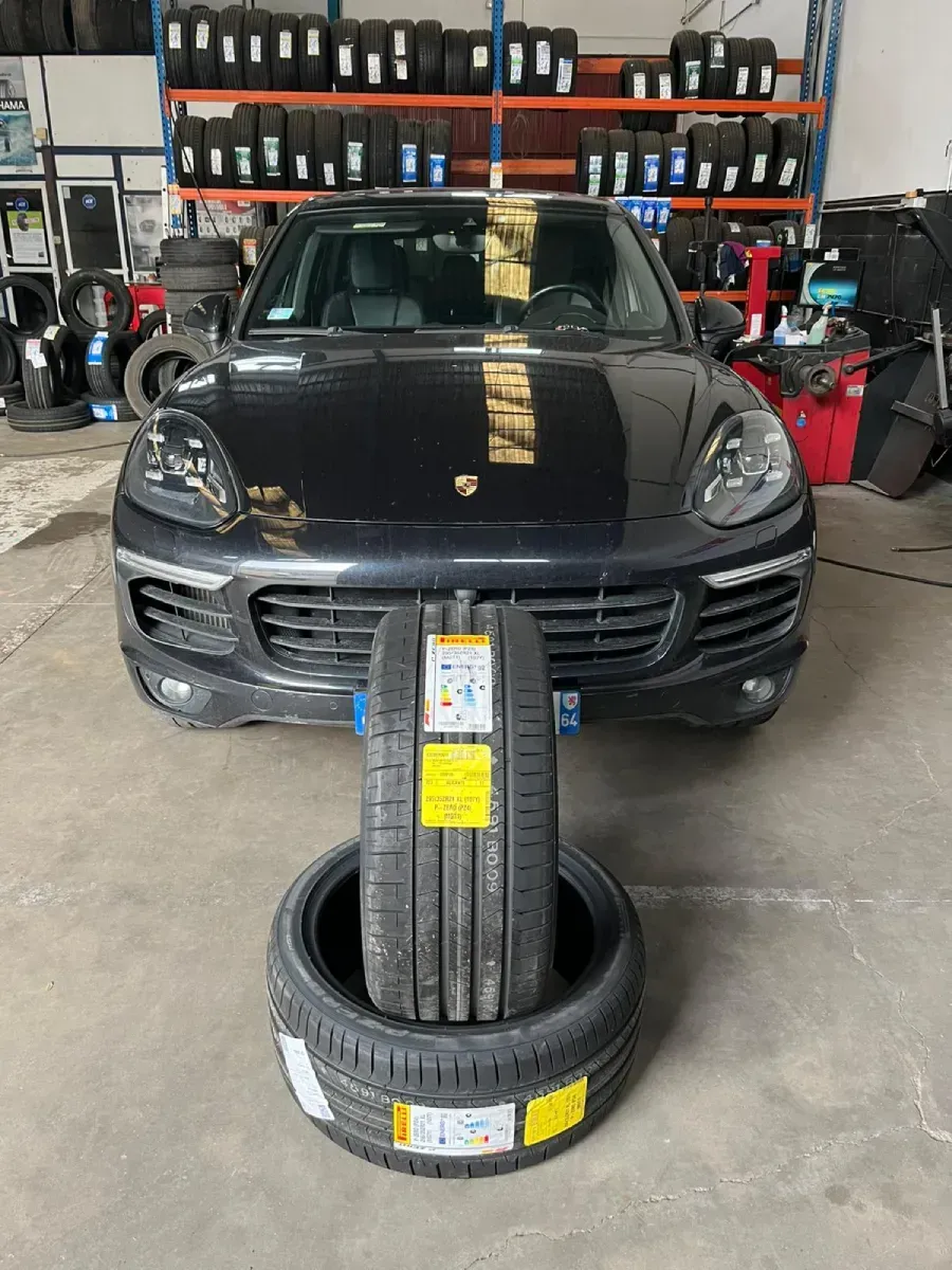 Una camioneta negra con llantas nuevas al frente, en una llantera. Llantas apiladas, estantes con más llantas visibles.