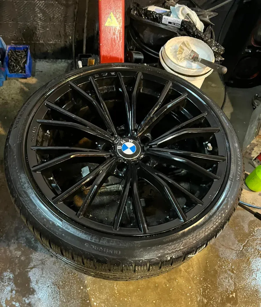 Rueda BMW negra con neumático, colocada sobre una superficie mojada, en un garaje.