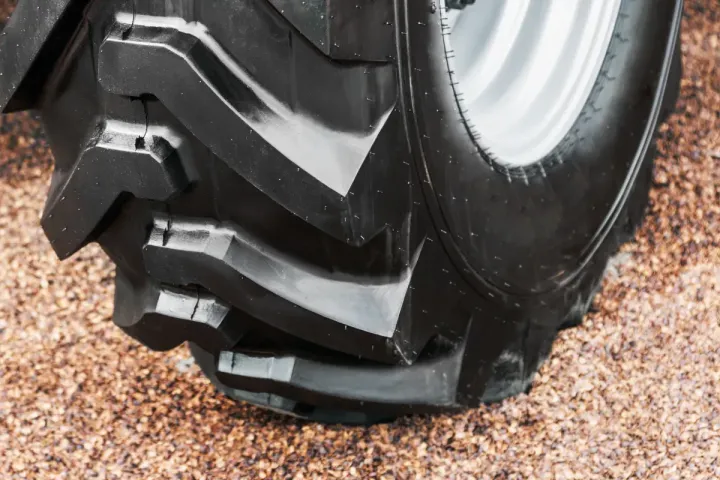 Primer plano de un neumático de tractor grande con huellas profundas, caucho negro, montado sobre una rueda plateada.