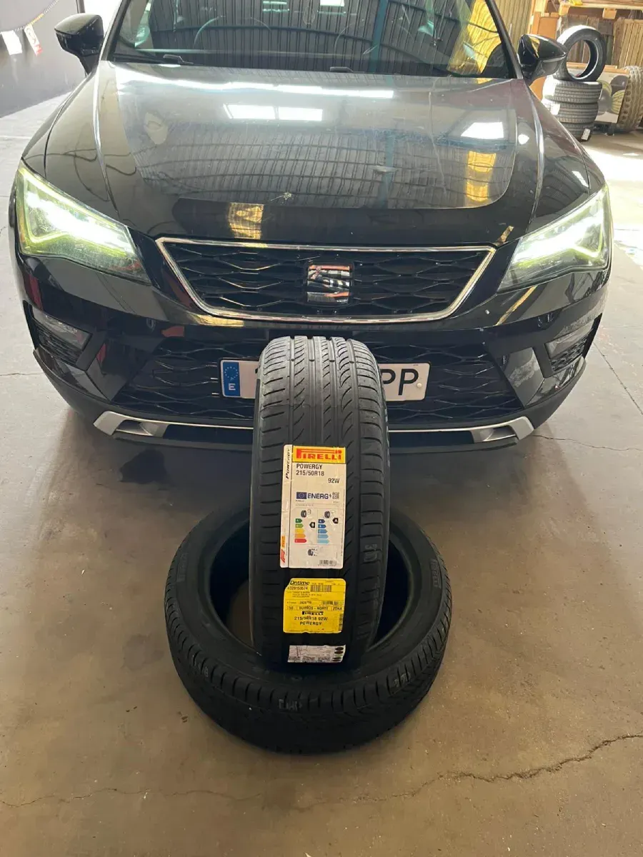 Coche negro con neumáticos nuevos delante. Los neumáticos tienen etiqueta de eficiencia energética.