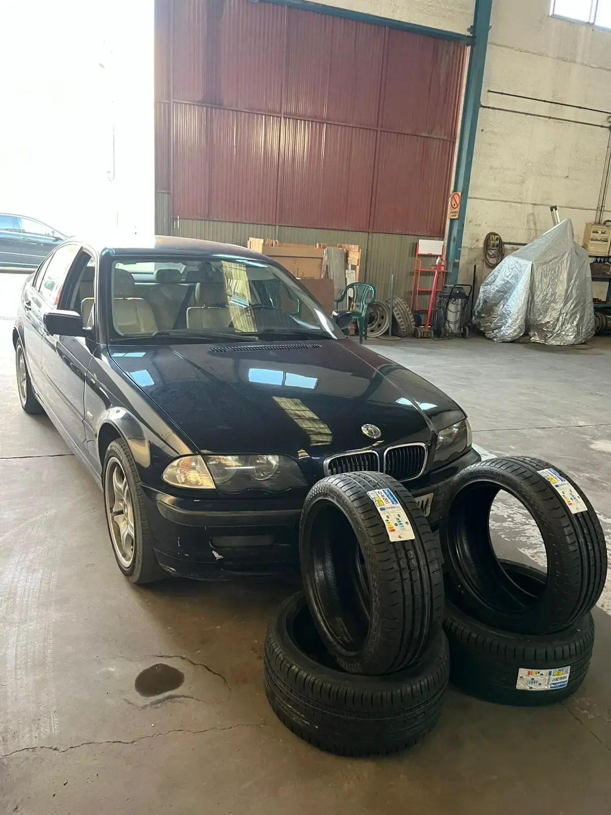 Sedán BMW negro con cuatro neumáticos nuevos en un garaje.