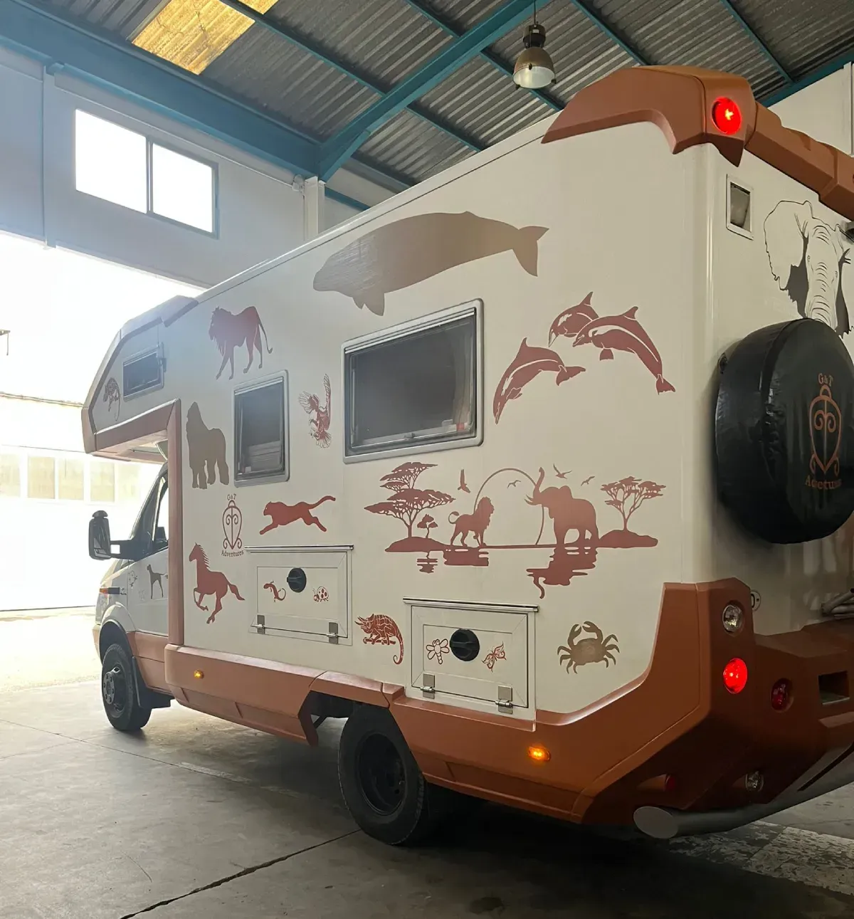 Autocaravana blanca y naranja con siluetas de animales aparcada en un garaje.