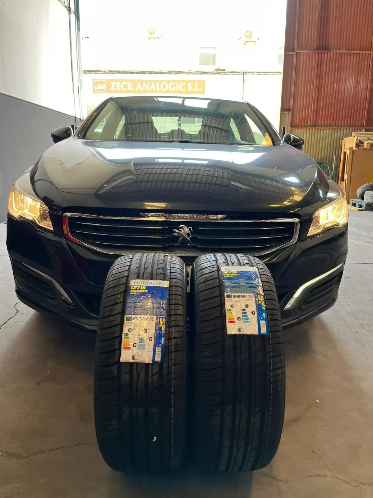 Coche Peugeot de color negro, con dos neumáticos nuevos delante, en el interior de un garaje.