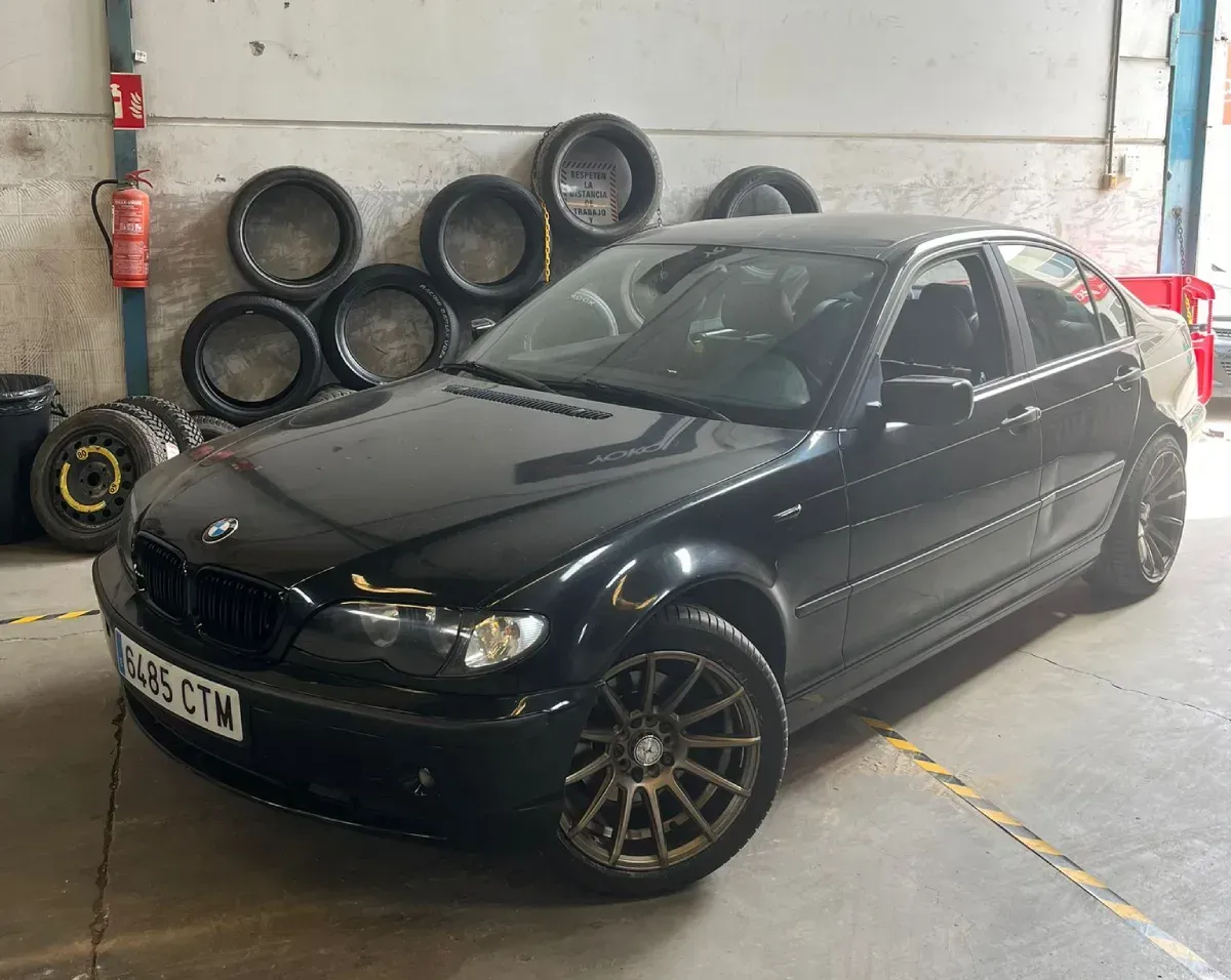 Un sedán BMW negro estacionado dentro de un garaje, con neumáticos apilados en el fondo.