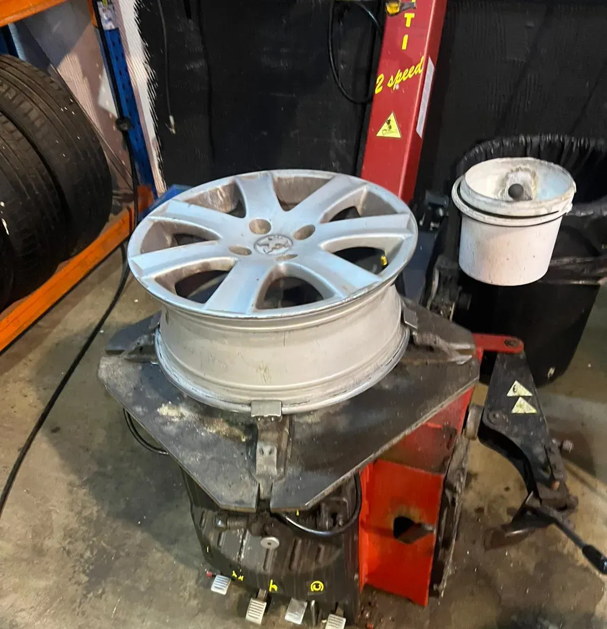 Rueda de coche plateada sobre una máquina para cambiar neumáticos en un garaje.