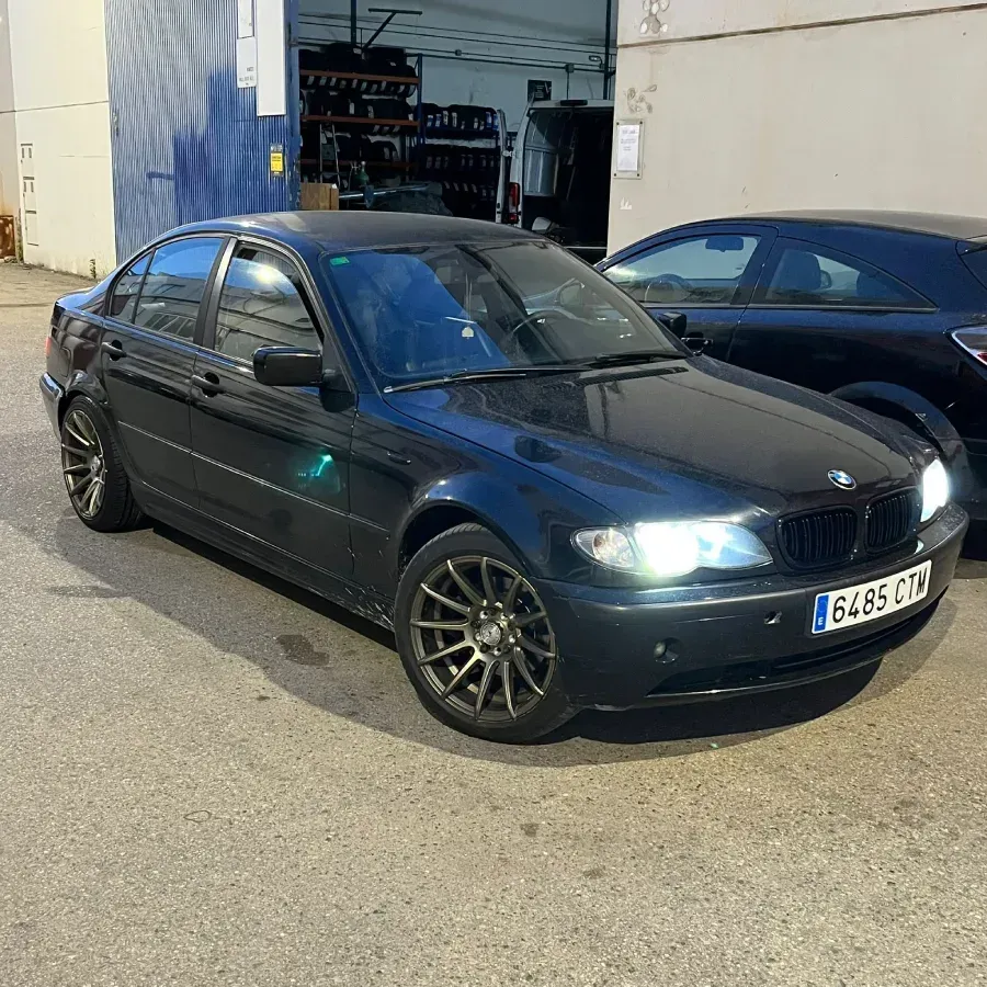 Un BMW sedán negro estacionado frente a un garaje, con una vista parcial de otro automóvil.