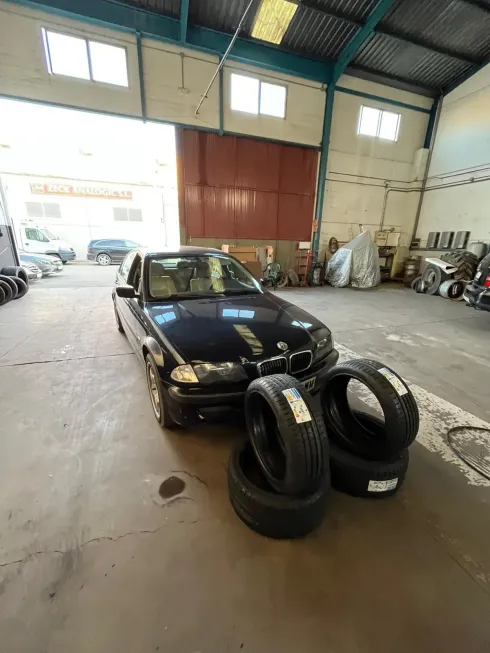 BMW sedán negro dentro de un garaje con cuatro neumáticos nuevos.