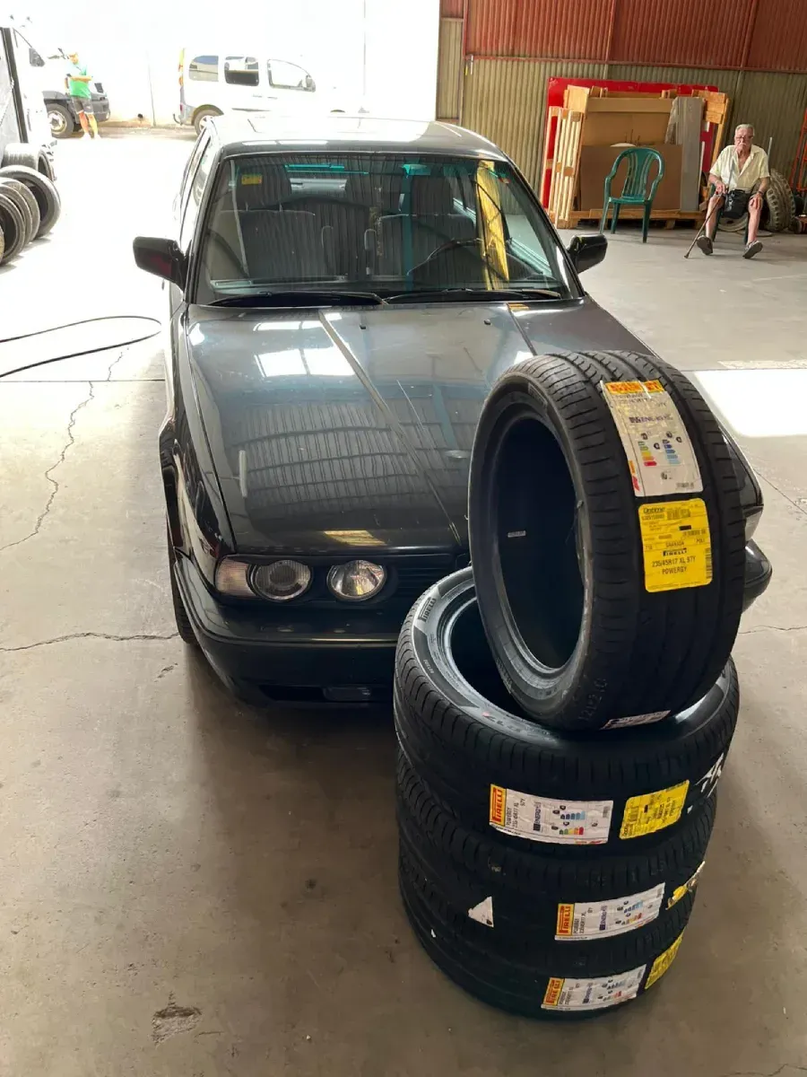 Un automóvil gris oscuro estacionado en un garaje con una pila de neumáticos nuevos en el frente.