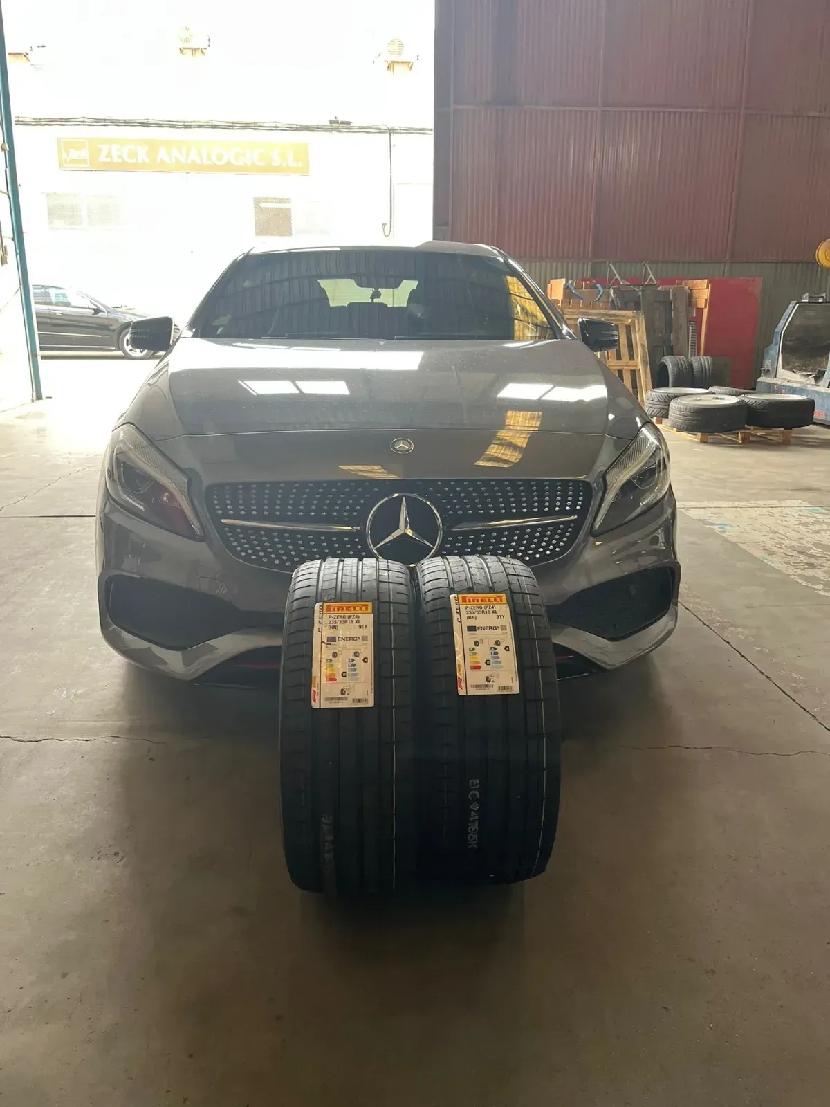 Dos neumáticos nuevos delante de un coche Mercedes-Benz gris en un garaje.