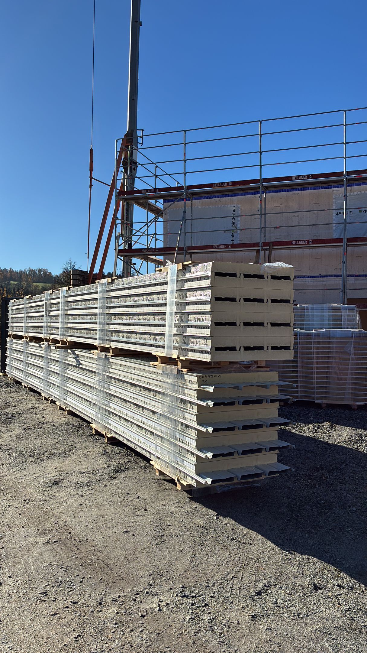 Übereinandergestapelte weiße Isolierpaneele auf einer Baustelle unter strahlend blauem Himmel.
