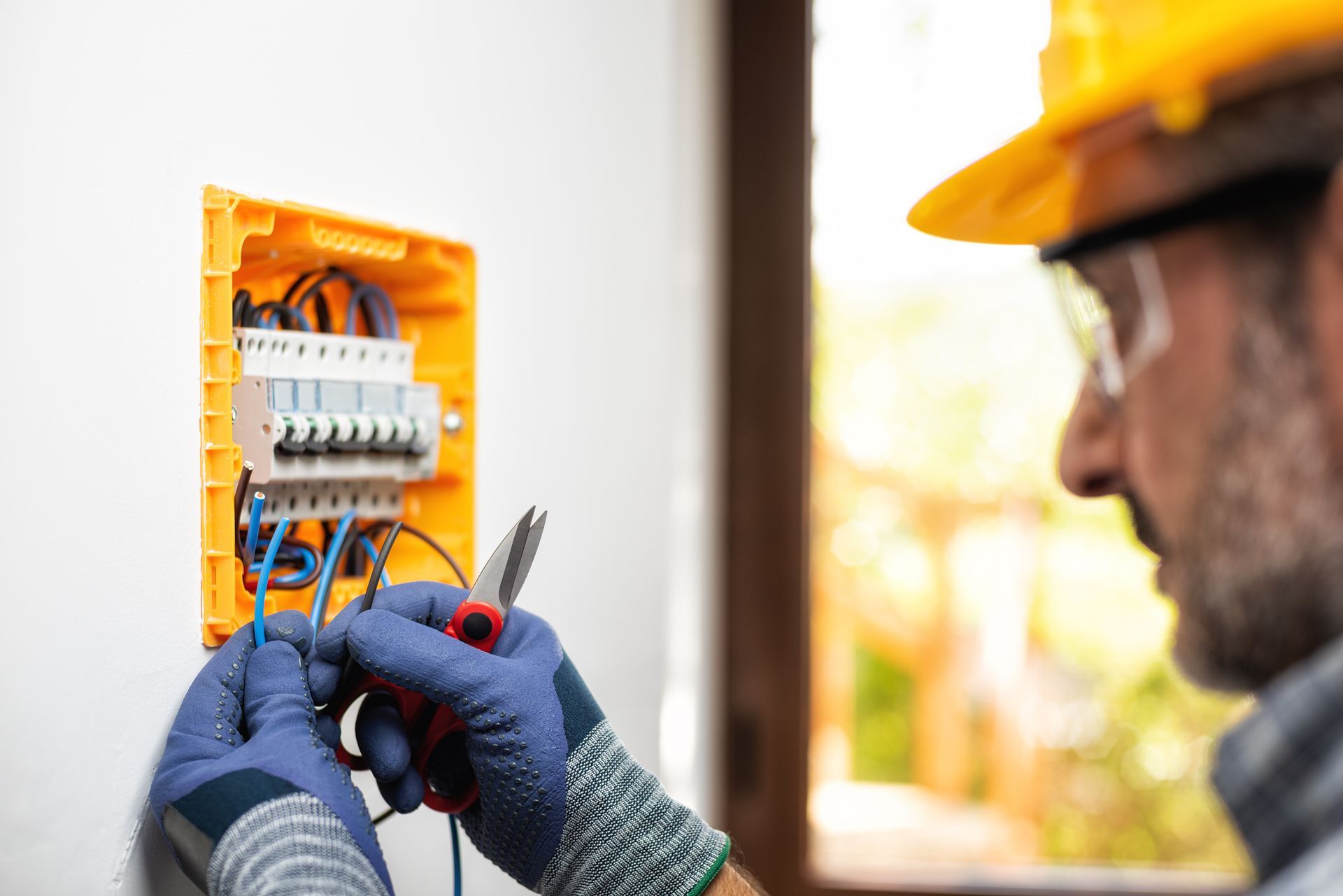 Électricien en train de travailler sur un boîtier électrique mural, manipulant des fils et des outils.