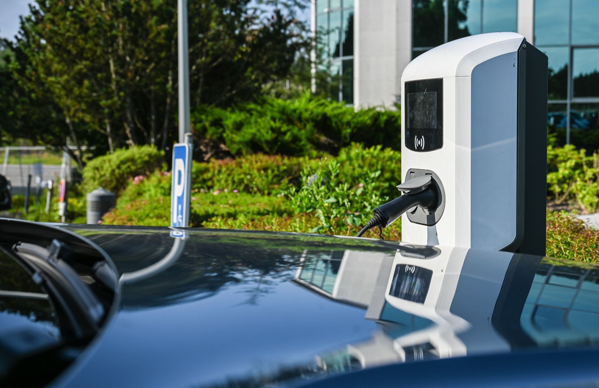 Borne de recharge pour véhicule électrique installée sur un parking, avec un câble branché sur une voiture.
