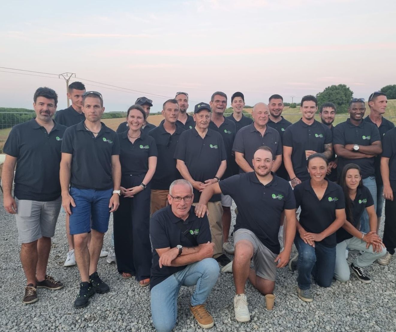 Arboriste en tenue de sécurité, travaillant dans un arbre. Tronc sombre, feuilles vertes, ciel bleu.