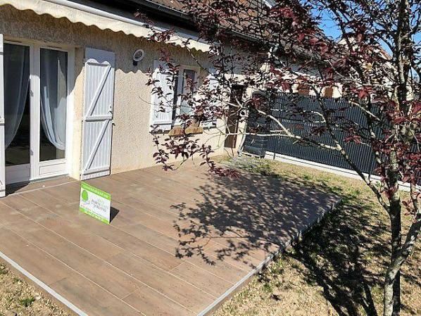 Terrasse en bois devant une maison aux volets blancs, un arbre aux feuilles rouges et un panneau solaire.