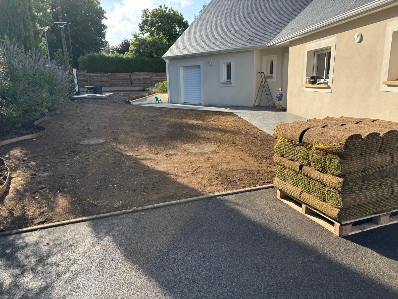 Une cour arrière résidentielle avec un lit de terre préparé, des rouleaux de gazon neufs et une maison.
