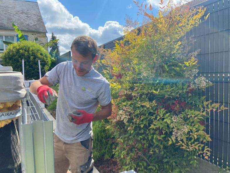 Un arboriste coupe une branche d'arbre à la tronçonneuse. Il travaille dans les branches, sur fond de ciel nuageux.