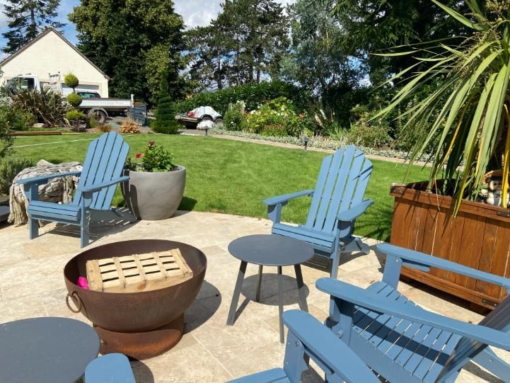 Des chaises Adirondack bleues disposées autour d'un foyer sur une terrasse, donnant sur une pelouse verdoyante.