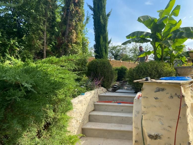 Des marches en pierre mènent à un jardin paysager à la végétation luxuriante, avec une personne en arrière-plan.