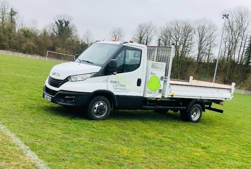 Camion paysagiste blanc stationné sur un terrain herbeux.