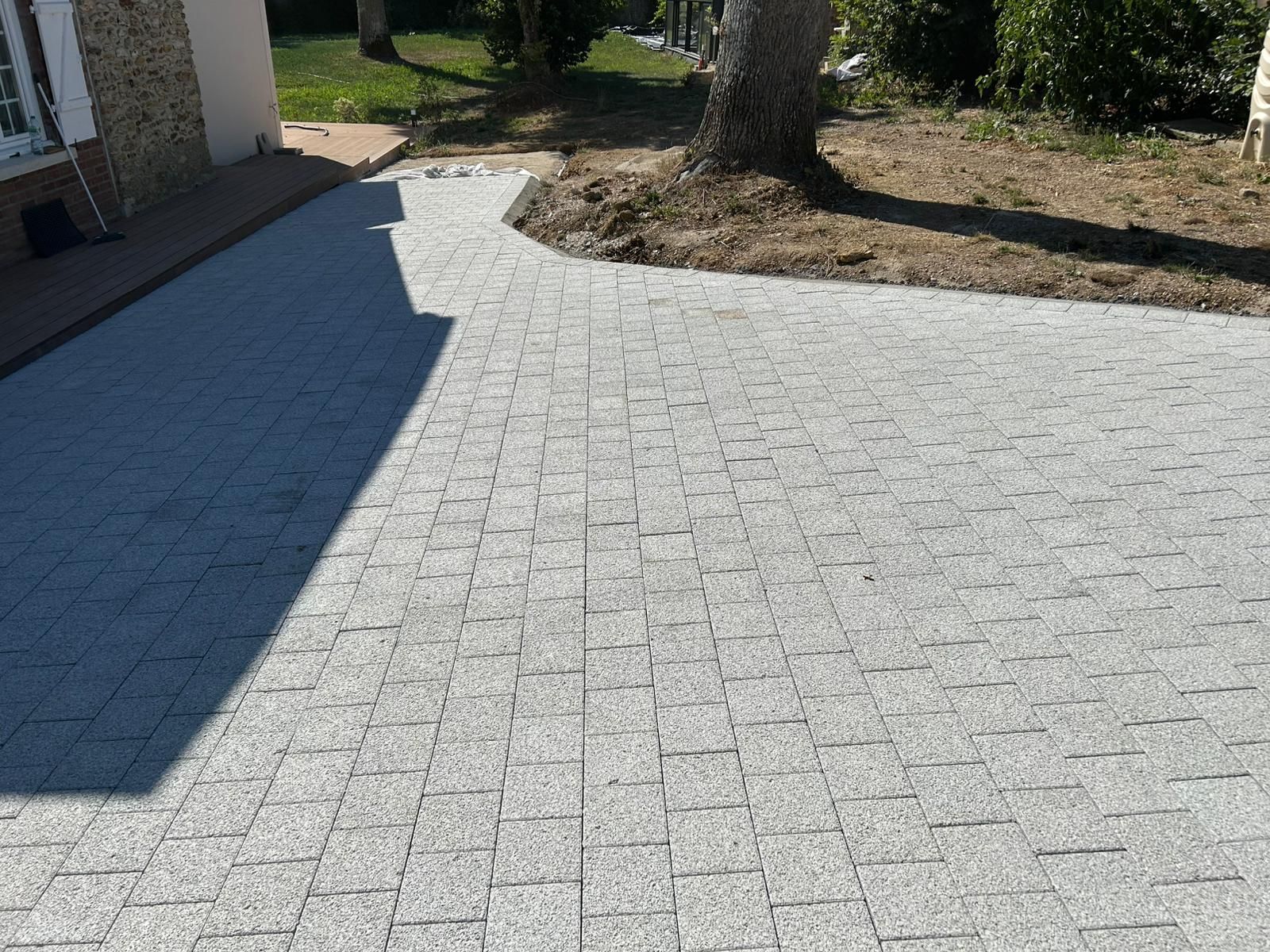 L'allée pavée de pavés gris contourne un arbre et se dirige vers une maison.