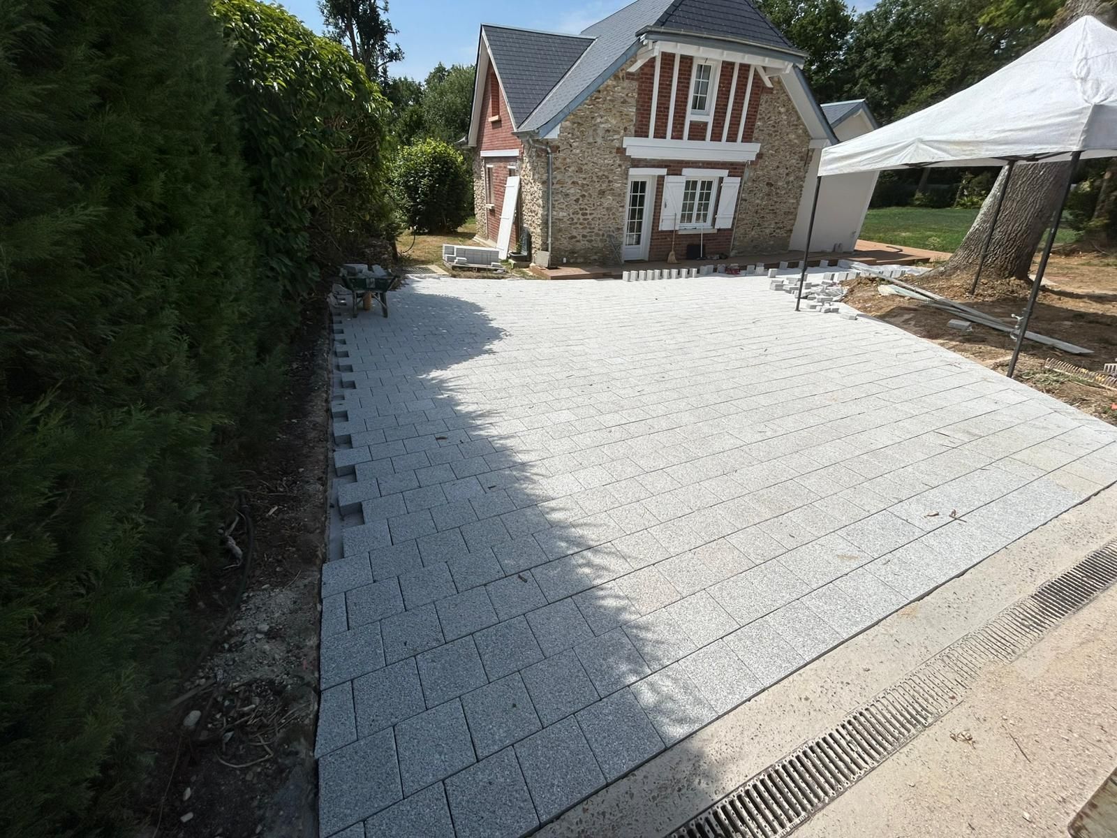 Allée nouvellement pavée de dalles rectangulaires grises devant une maison en pierre.