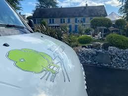 Une camionnette blanche avec un logo représentant un arbre vert est garée devant une grande maison.