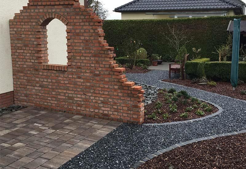 In einem Garten steht eine Backsteinmauer mit einem Loch darin.