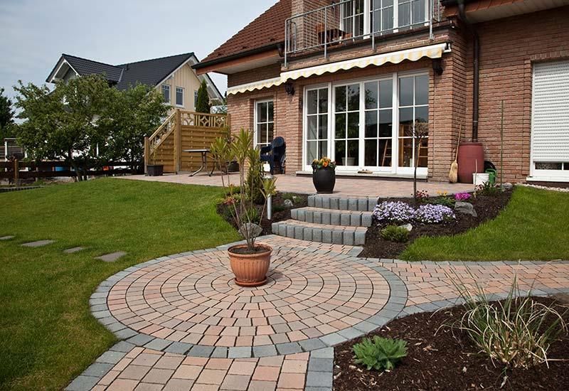 Ein gemauerter Gehweg führt zu einer Terrasse vor einem Haus