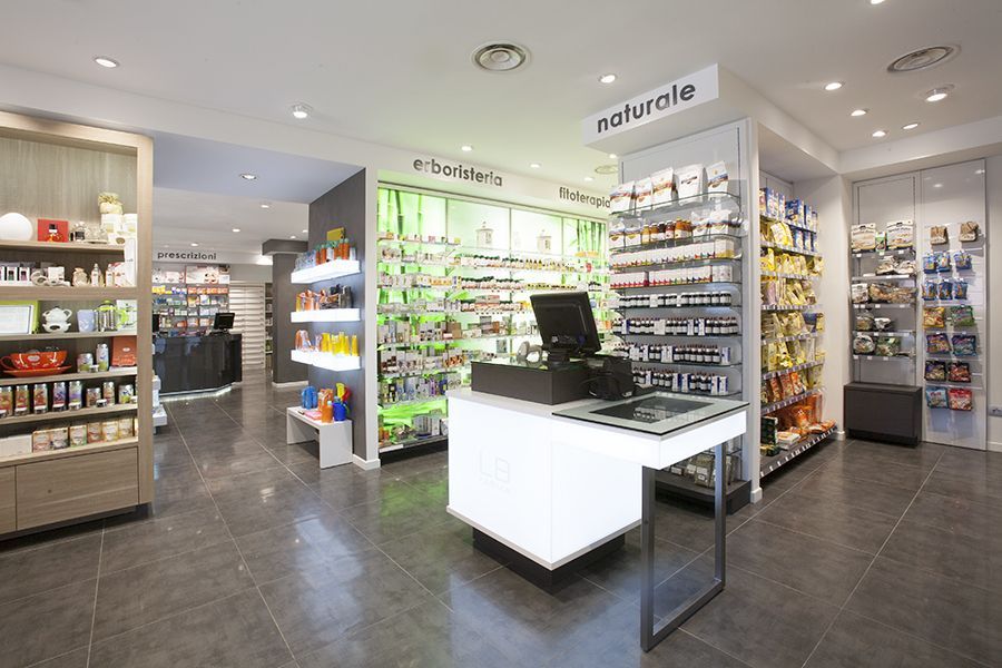 Interno luminoso della farmacia, con scaffali pieni di prodotti e un bancone espositivo bianco al centro