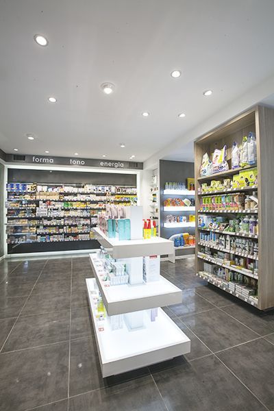 Corsia luminosa della farmacia al dettaglio con scaffali di prodotti per l’igiene personale, espositori bianchi e pavimento in piastrelle scure