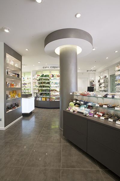 Interno moderno della farmacia con scaffali bianchi, vetrine in vetro e una colonna rotonda al centro.