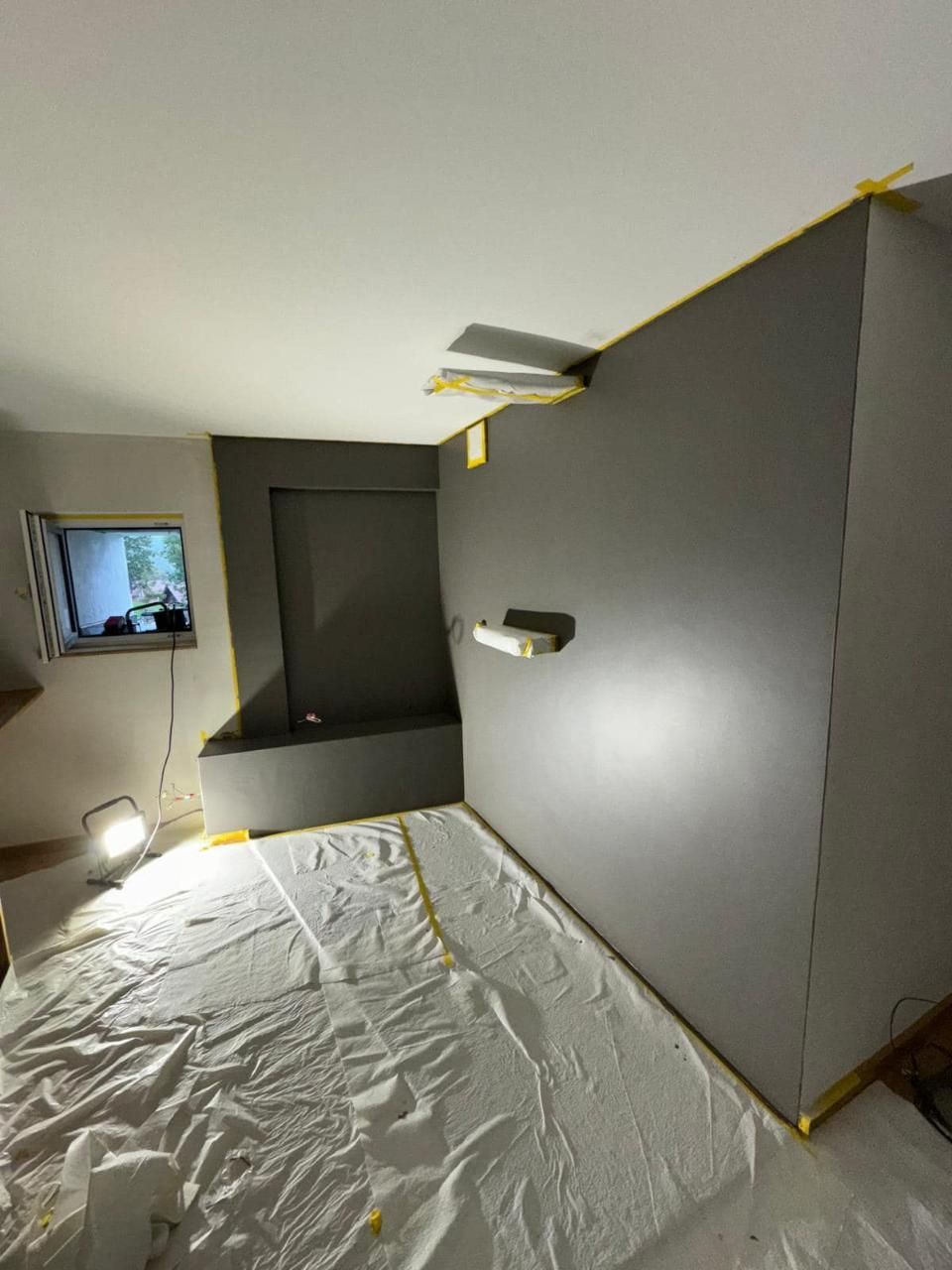 Une pièce avec un mur gris et un drap blanc sur le sol.