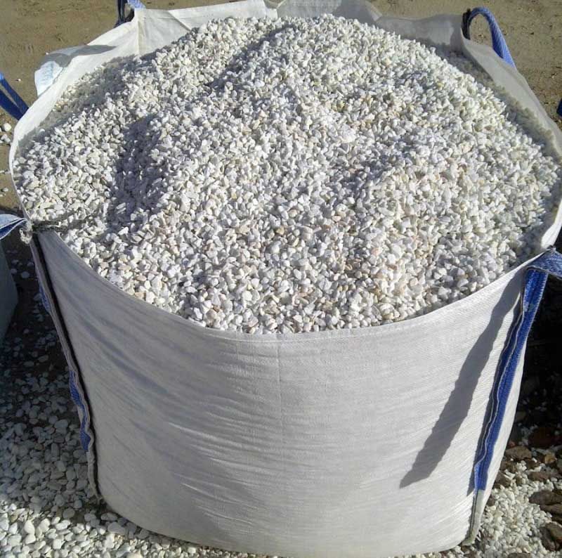 Gran saco blanco a granel lleno de pequeñas piedras blancas o grava al aire libre