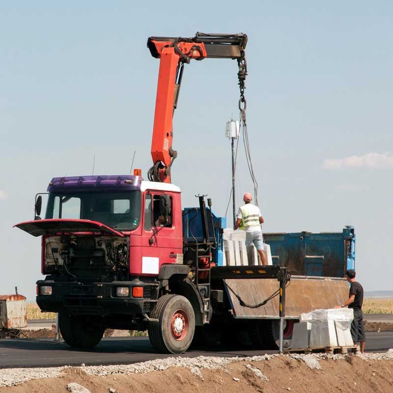 Camión grúa descargando materiales en una obra de construcción con trabajadores cerca.